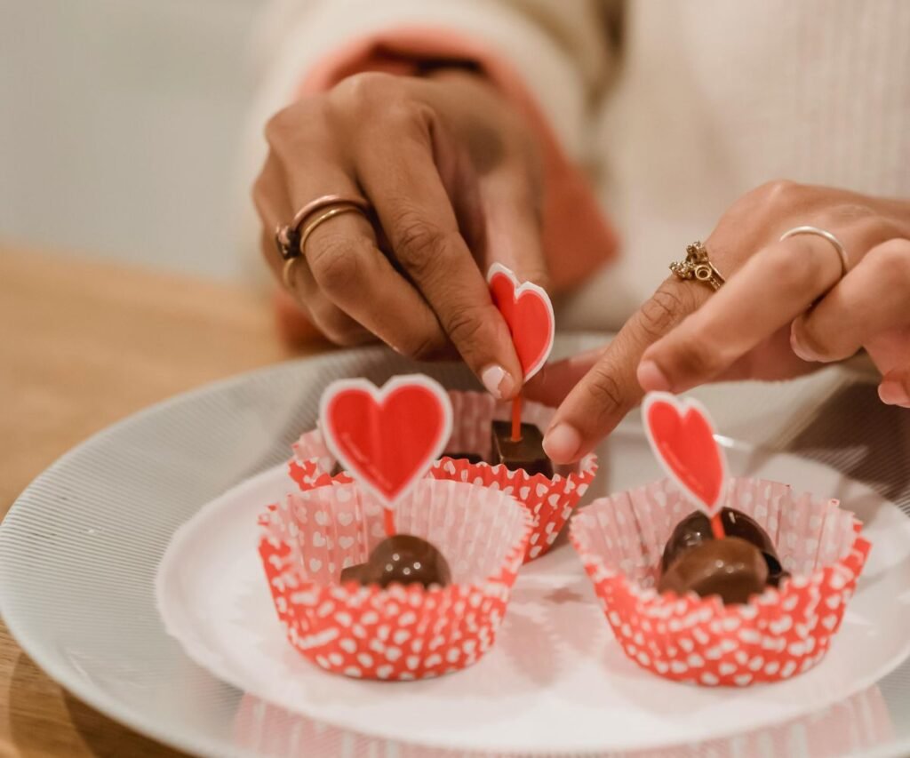 Woman decorating Valentine's Day chocolate cupcakes with red heart toppers in pink polka dot wrappers