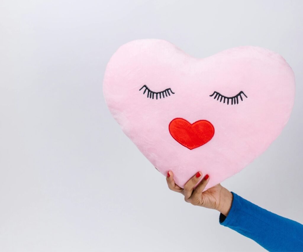 Woman holding pink heart-shaped pillow with eyelashes and red lips design for Valentine's Day gift
