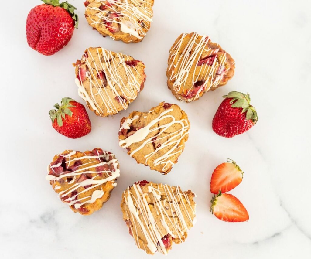 Heart-shaped strawberry scones with white chocolate drizzle and fresh strawberries on marble surface